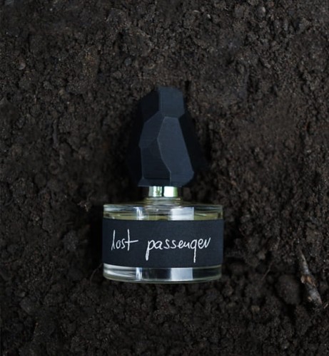 Ilustracja dla zapachu yDe Lost passenger, butelka perfum leży na świeżej rozkopanej czarnej ziemii.